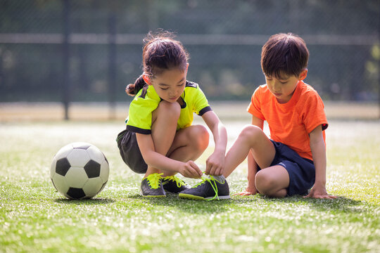 Little girl helping her brother to tie shoelace on soccer field