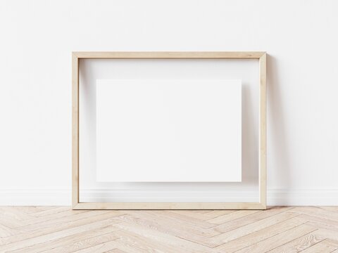Rectangular wooden picture frame with thin light border and white background standing on wooden floor. 3D Illustration.