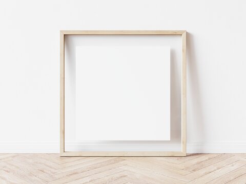 Empty square picture frame with light wood border standing on wooden floor leaning on white wall. 3D Illustration.