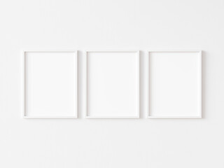 Three blank vertically oriented rectangular picture frames with thin white border hanging on white wall. 3D illustration.