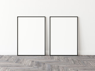 Two empty vertically oriented rectangular picture frames with thin black border standing on wooden parquet floor leaning on white wall. 3D Illustration.