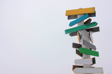 Multicolored handmade crossroad signpost on white sky background. Close-up of arrow sign