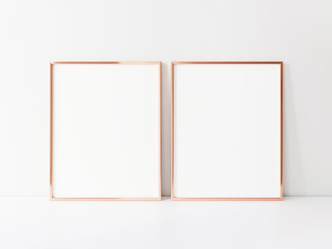 Two empty vertically oriented rosegold frames stand on the white table top. 3d Illustration.