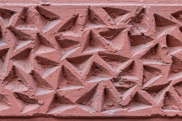 The corrugated surface of a plastered concrete wall covered with triangular depressions and recesses.