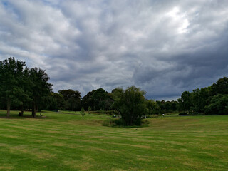 Obraz na płótnie Canvas Beautiful morning view of a park with green grass, tall trees and dark cloudy sky, Fagan park, Galston, Sydney, New South Wales, Australia 