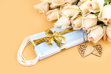 Bouquet of roses, wooden decorative hearts and protective masks with golden ribbon and bow on pastel background, flat lay. Gift for Wedding, Mother's Day, Valentine's day during coronavirus pandemic.