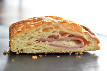 Croissant with ham and cheese on a black plate.
