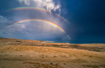 Fototapeta na wymiar Beautiful Israeli landscape: rainbow in the clouds over the Dead Sea, the lowest place on Earth, its north-western shore covered in sinkholes