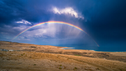 Fototapeta na wymiar Beautiful Israeli landscape: rainbow in the clouds over the Dead Sea, the lowest place on Earth, its north-western shore covered in sinkholes