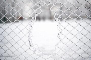 Hole in the steel mesh in winter. Snow and ice.