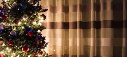 A Christmas tree decorated with lights and balls in front of a striped curtain (Marche, Italy,...