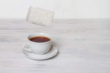 A huge lump of sugar falls into a Cup of tea. White background. Copy space.