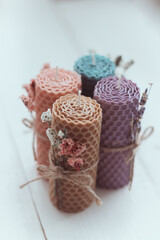 Close up of gift set of four colored  natural decorative  beewax candles with dried flowers and a honey aroma for interior and tradition on a white table. Selective focus. A delicate color palette