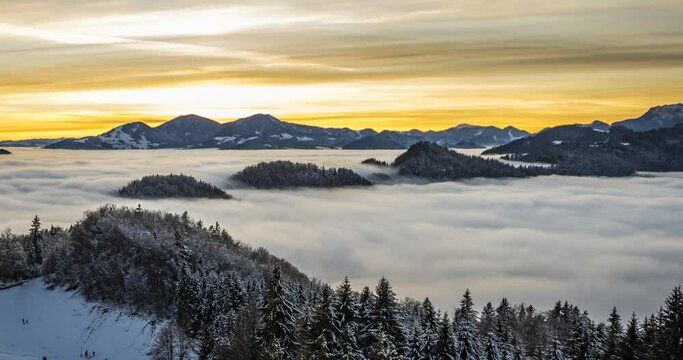 Time lapse of inversion clouds moving in valley, Slovenia. Colorful sunset with snow covered mountains. Kids sledding on snowy slope on the hill. Left truck parallel moving, wide angle, elevated view