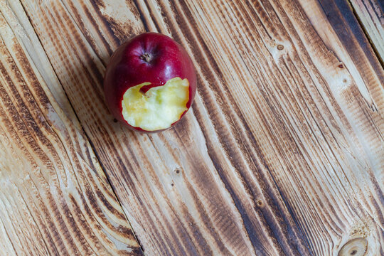 A Red Apple With A Tooth Mark On A Wooden Background.