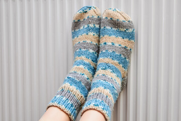 A girl in blue woolen socks warms her feet on the radiator