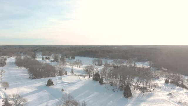 A crawling slow drone shot of a snow-covered golf course showing the indents of course features, trees, and the peaceful landscape.