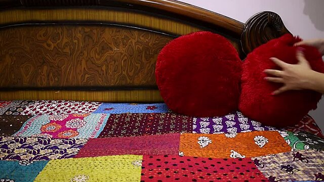 woman making over bed adjusting red velvet pillow on bed