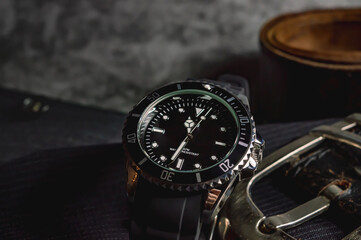Fototapeta premium Close-up of a black-chrome watch, a belt buckle of a leather belt on top of gray fabric