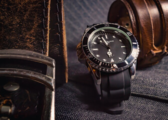 Close-up of a leather belt, a black and chrome watch and a leather bracelet on top of gray fabric