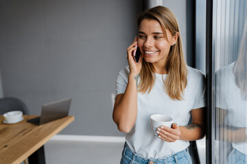 Beautiful happy girl talking on mobile phone and drinking coffee