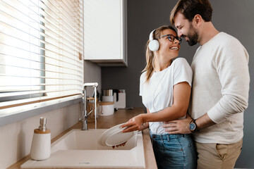 Beautiful cheerful couple smiling and hugging while washing dishes