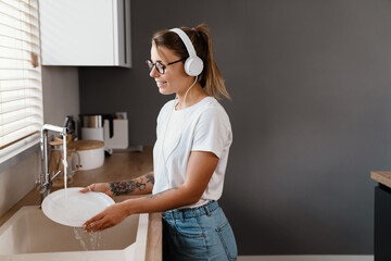Beautiful cheerful girl in headphones smiling and washing dishes
