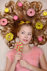 Vertical portrait of a young cute girl lying on a background of colorful donuts and sweets. Top view. Studio