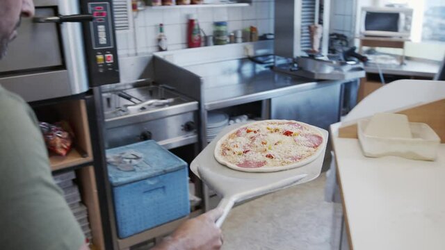 Placing Pizza in Pizza Oven using a pizza peel Slow motion shot. Chef cooking pizza at Italian restaurant.