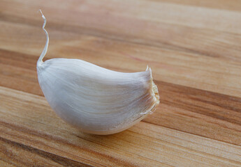 A slice of garlic lies on a wooden board.