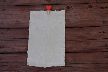 A sheet of parchment paper with a clothespin with a red heart on a wooden background. Copy the space