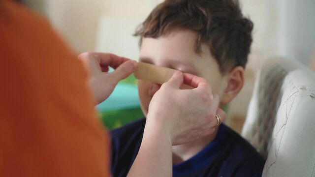a woman sticks a plaster on the wound of a child. the boy who injured his face receives medical care at home. deep wound on the nose and bruises with scratches on the face.