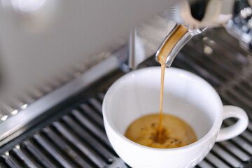 Closeup espresso pouring to white cup from coffee machine, selective and soft focus