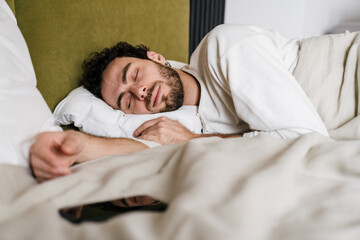 Peaceful man sleeping with mobile phone while lying in bed