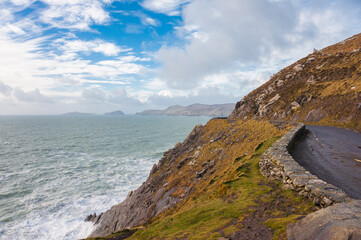 Dark wet road above cliffs going far in Ireland Dingle head near Atlantic ocean in a cloudy day in winter and autumn. Concepts: season, outdoors, travel, landscape