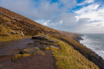 Dark wet road above cliffs going far in Ireland Dingle head near Atlantic ocean in a cloudy day in winter and autumn. Concepts: season, outdoors, travel, landscape