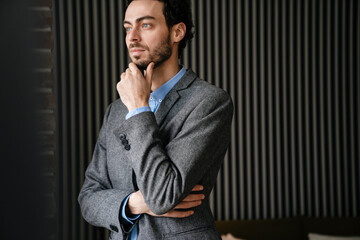 Confident pleased businessman in jacket posing and looking aside indoors