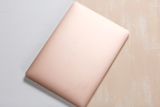 The laptop is pink. The surface is painted in white and beige. Filmed from above.