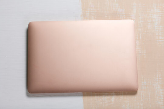The laptop is pink. The surface is painted in white and beige. Filmed from above.