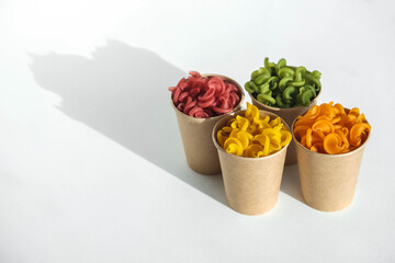 Multicolored pasta in a disposable kraft paper cups on a white background. Top view. Copy, empty space for text