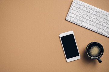 Minimalist workspace with computer keyboard, smartphone with blank screen mockup, cup of coffee on brown background. Top view with copy space.