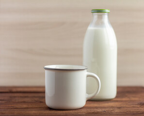 A bottle of milk and a mug on a wooden table.