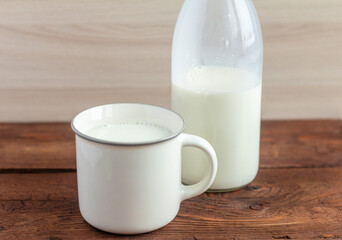 A bottle of milk and a mug of milk on a wooden table.