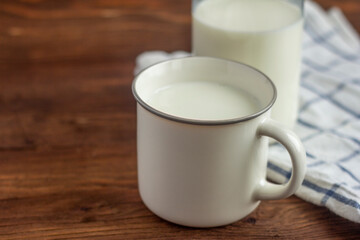 A bottle of milk and a mug of milk on a wooden table.