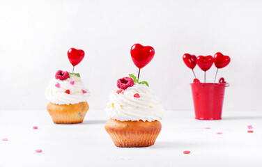 Cupcakes topped with whipped cream, heart shaped sprinkles and toppers and raspberry on the white table. Dessert for Valentine Day or wedding