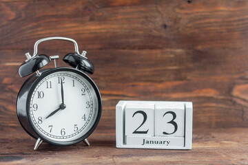 January 23 on a white calendar, next to a retro alarm clock on a dark wooden background.Calendar for January.A copy of the space.