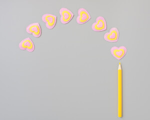 Yellow pencil and pink-yellow hearts on a gray background. Happy Valentines Day.
