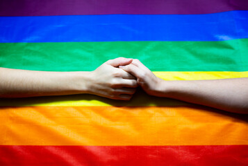 Lgbt community colorful flag. Two women's hands on rainbow background. Lesbian and gay problems. Legalization of marriage for couples with homosexual orientation.