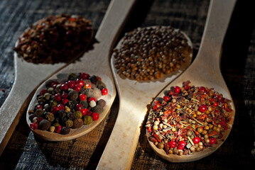 A mixture of various spices in a wooden spoon. Spices and seasonings on an old shabby board. Mix on a pile close up. Contrasting dramatic light as an artistic effect.