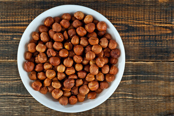 Hazelnuts in a white bowl on an old shabby board. Nuts on a brown wooden table.